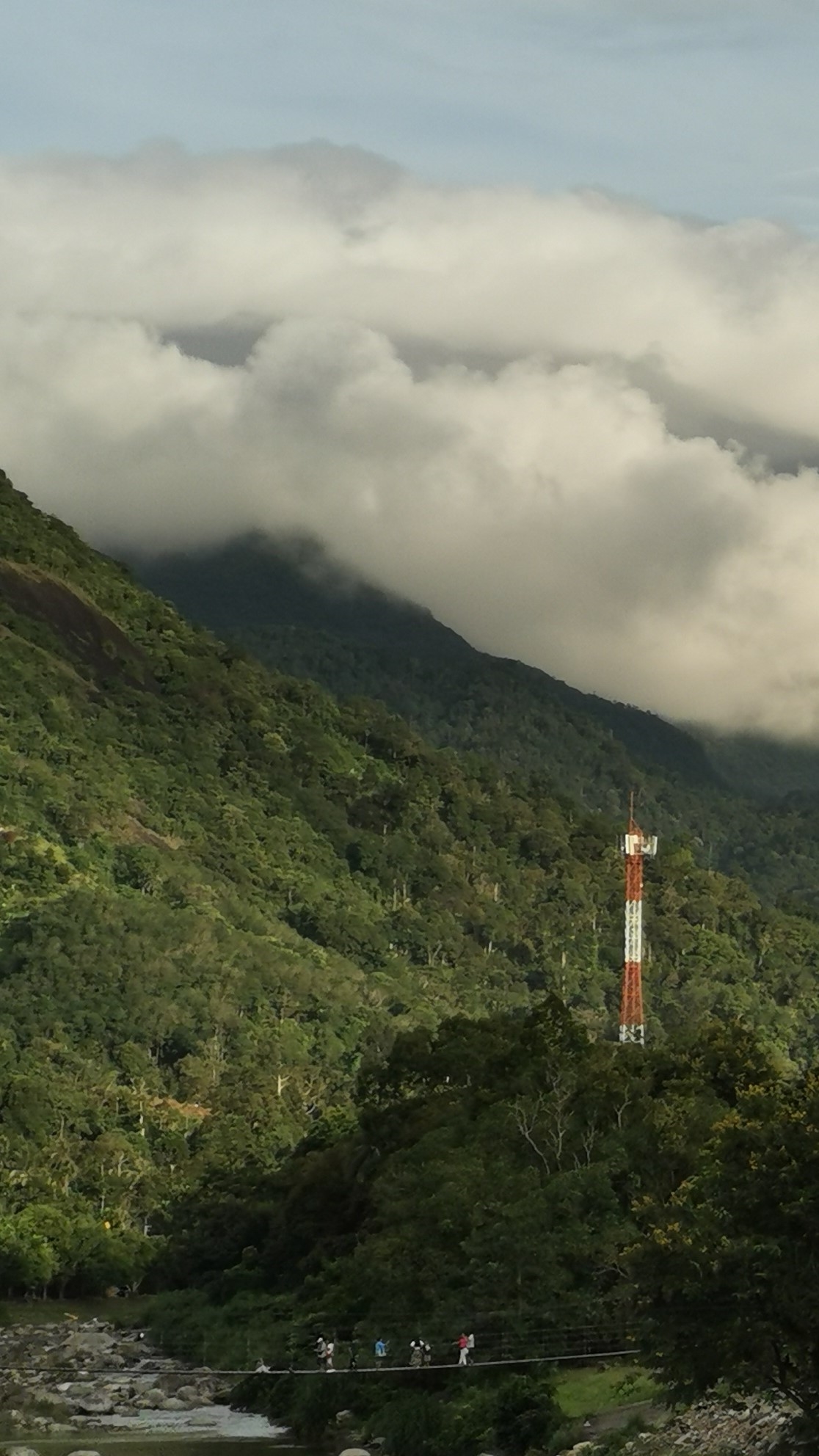 Morning's First Light: Double cloudbelt formation hugging the green ridgelines over Wat Khiri Wong and the market rope bridge at dawn.